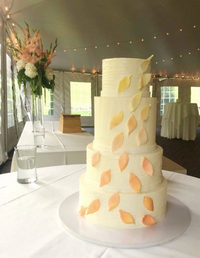 4-tier buttercream covered wedding cake with a tall tier and yellow to peach gumpaste leaves cascading down the front