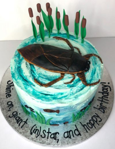birthday cake with giant water bug on top and buttercream water with small fish and cattails