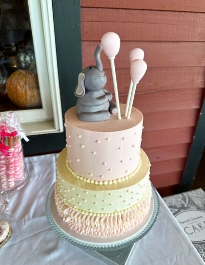 2-tiered white and light pink cake with sitting fondant elephant and 3 fondant balloons on top