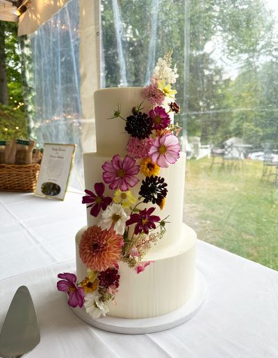 3-tier wedding cake with tall tier in the middle and wildflowers on the side on a table at the West Mountain Inn